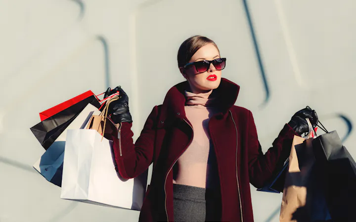 A shopper in sunglasses carrying paper bags from designer stores