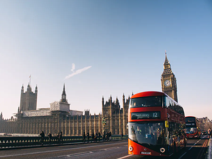 A red double-decker bus crossing Westminster Bridge towards Big Ben on a sunny day
